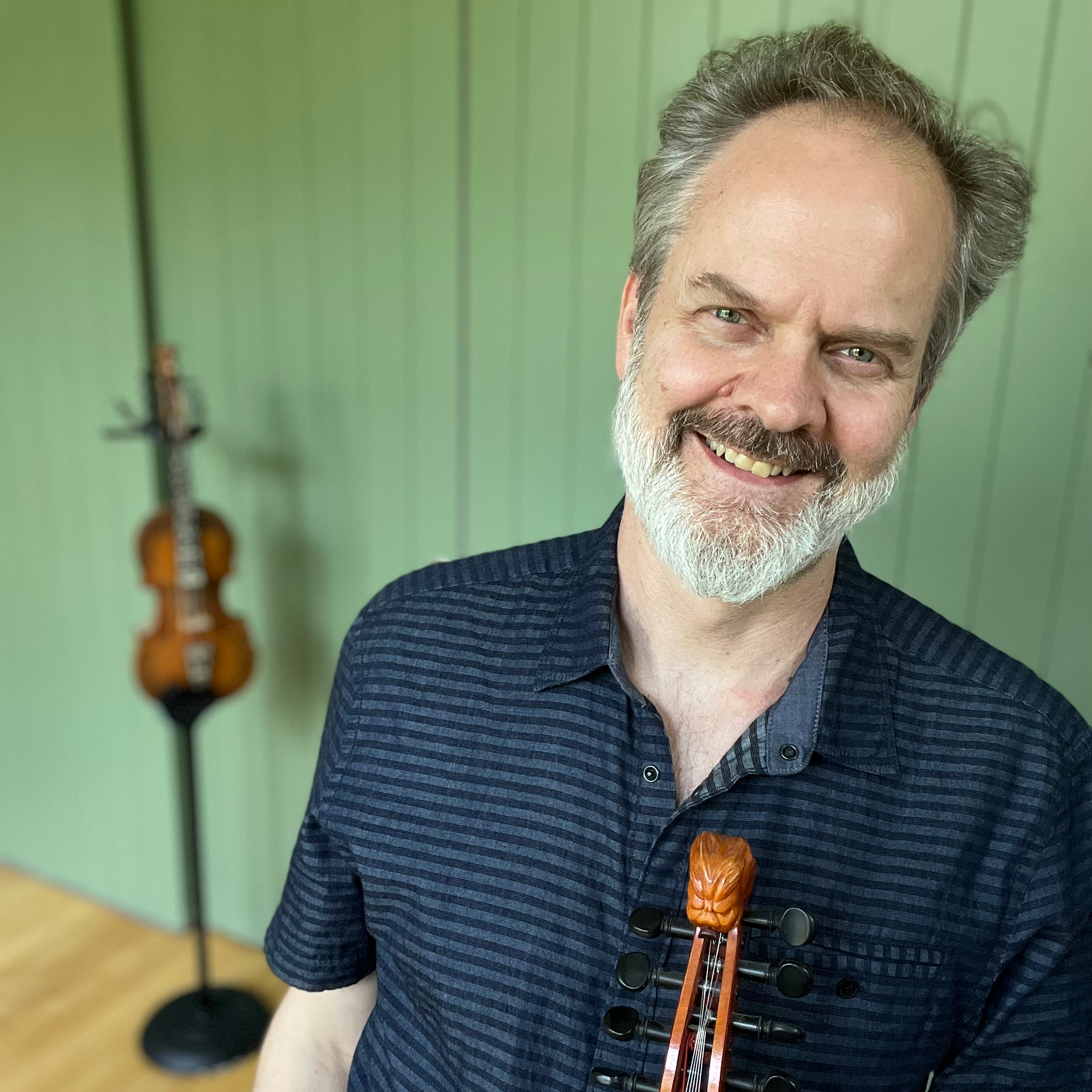 Headshot of Dan Trueman smiling and holding a fiddle.