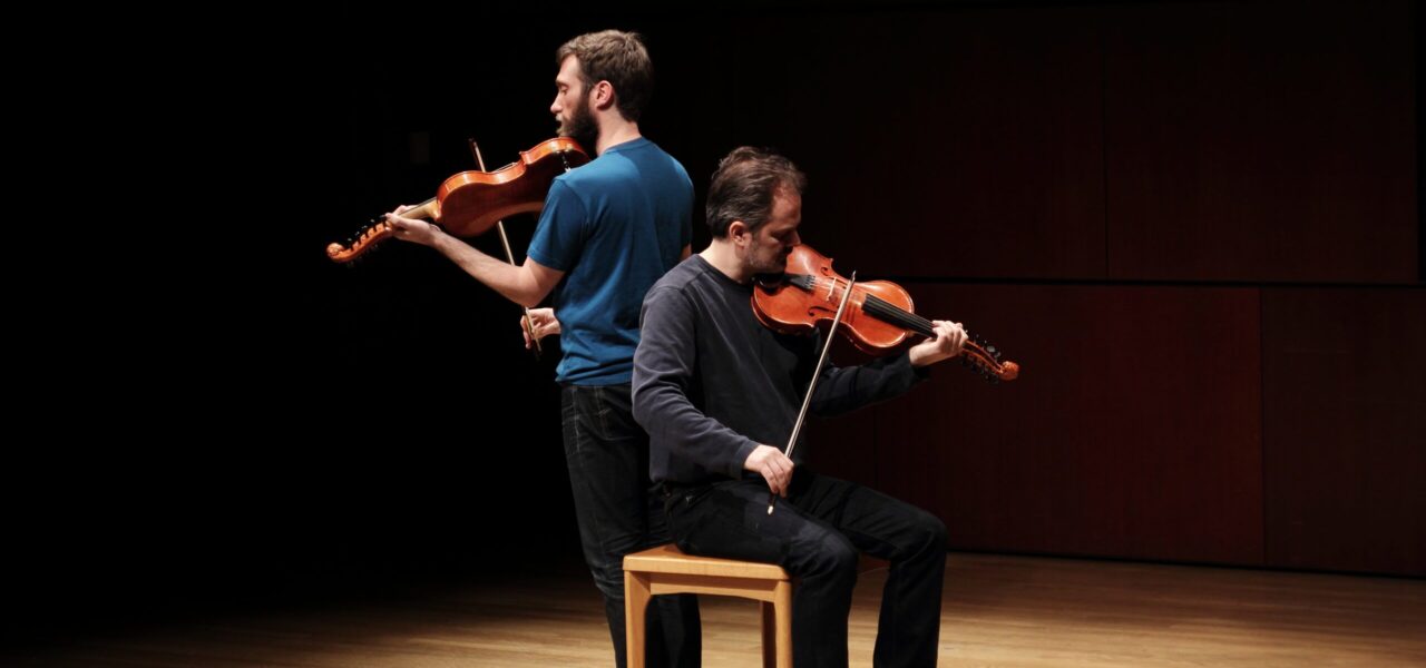 photo of Caoimhín Ó Raghallaigh and Dan Trueman, playing instruments on a darkened stage.