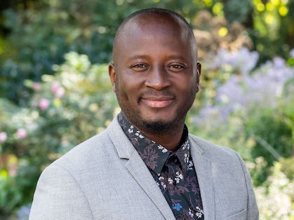 Headshot of Olivier Tarpaga, smiling, with an outdoor background of bushes and flowers