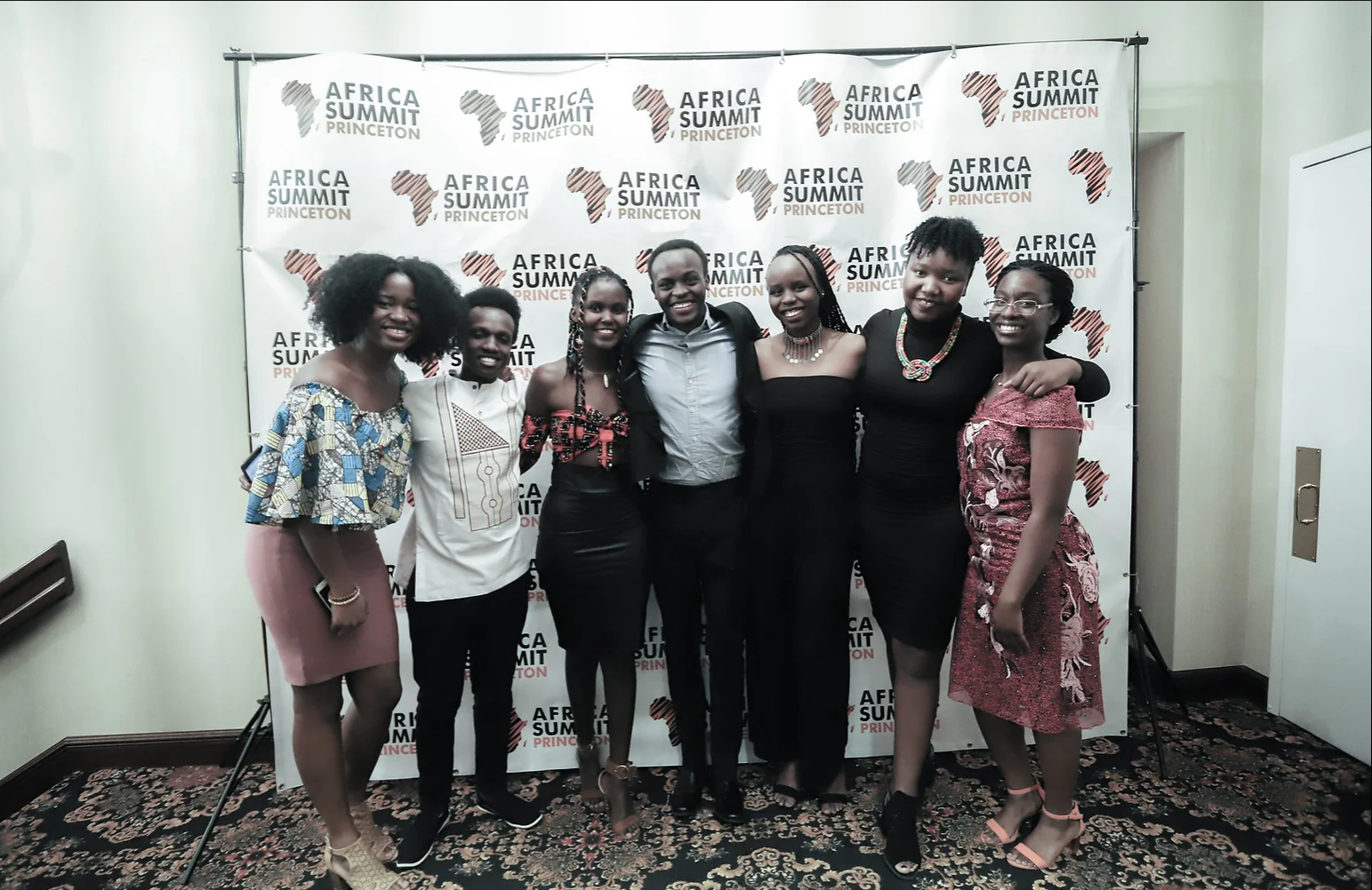 7 people smiling and standing in front of a backdrop curtain that reads "Africa Summit Princeton"
