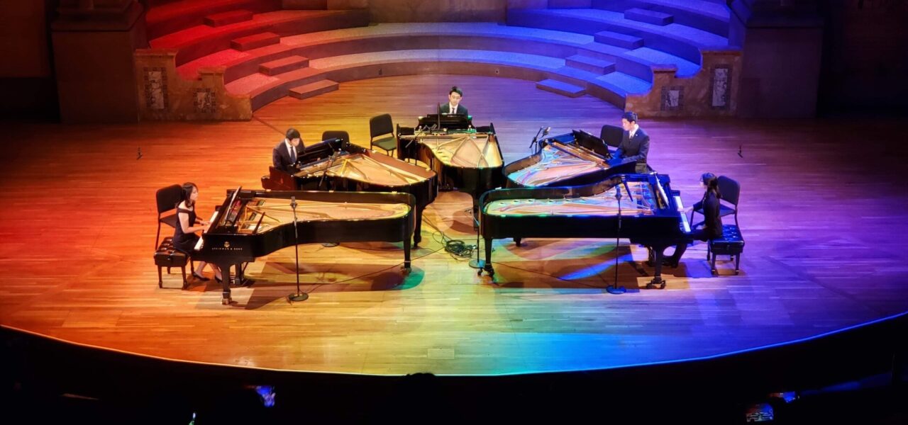 5 large pianos on stage at the same time, with pianists performing