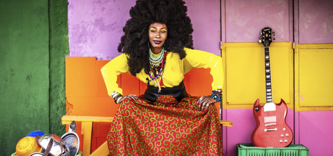 A person dressed in colorful yellow top and orange bottom with a purple background