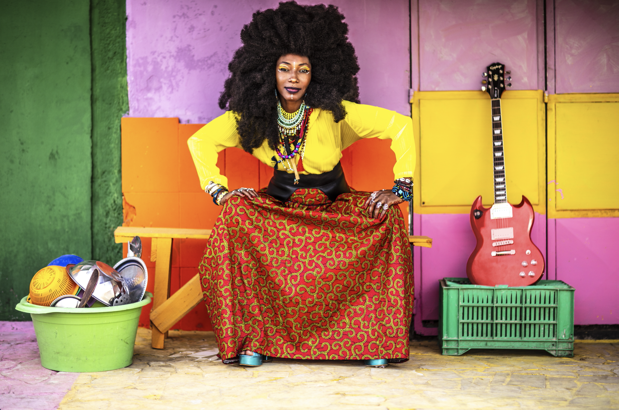 A person dressed in colorful yellow top and orange bottom with a purple background