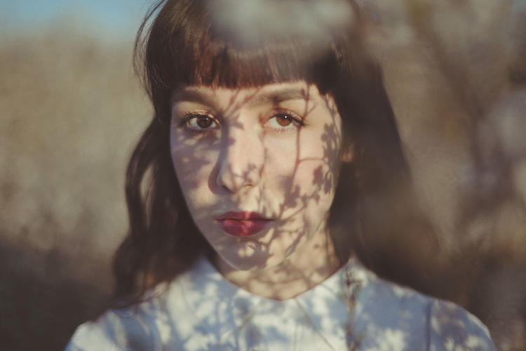 Artsy headshot of Alkyone with shadows of branches overlaying her face